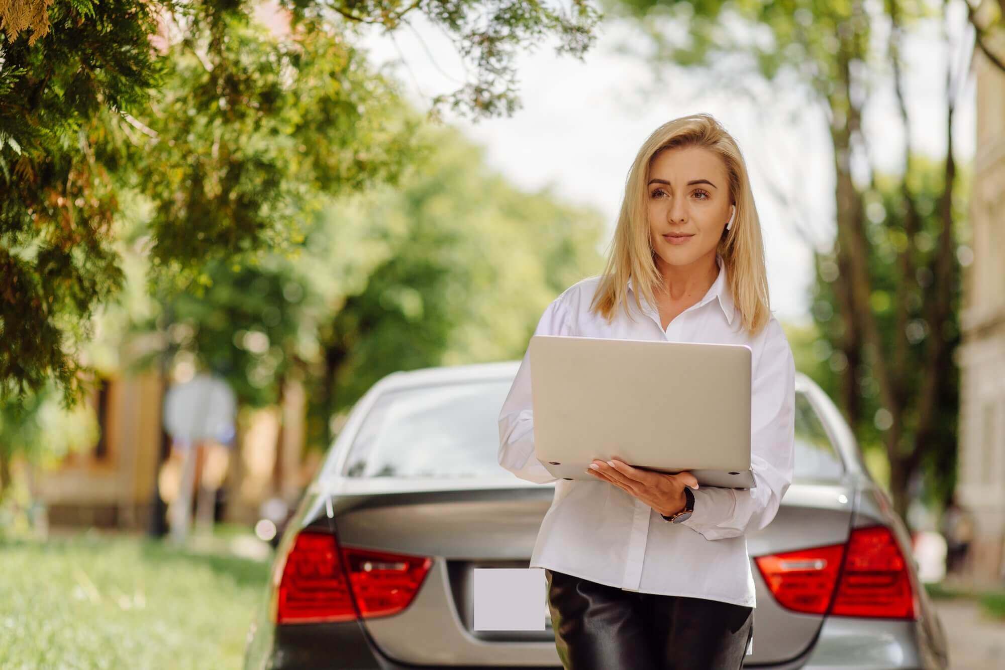 Woman stood by car boot holding her laptop